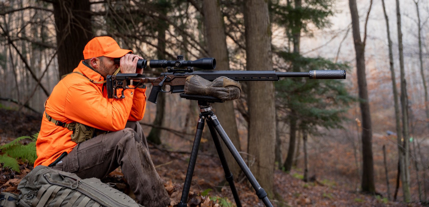 Hunting with a TiTrex® Suppressor Hunter in the woods wearing a bright orange jacket and hat looking for hunting game with a christensen rifle on a bipod with a TiTrex® suppressor